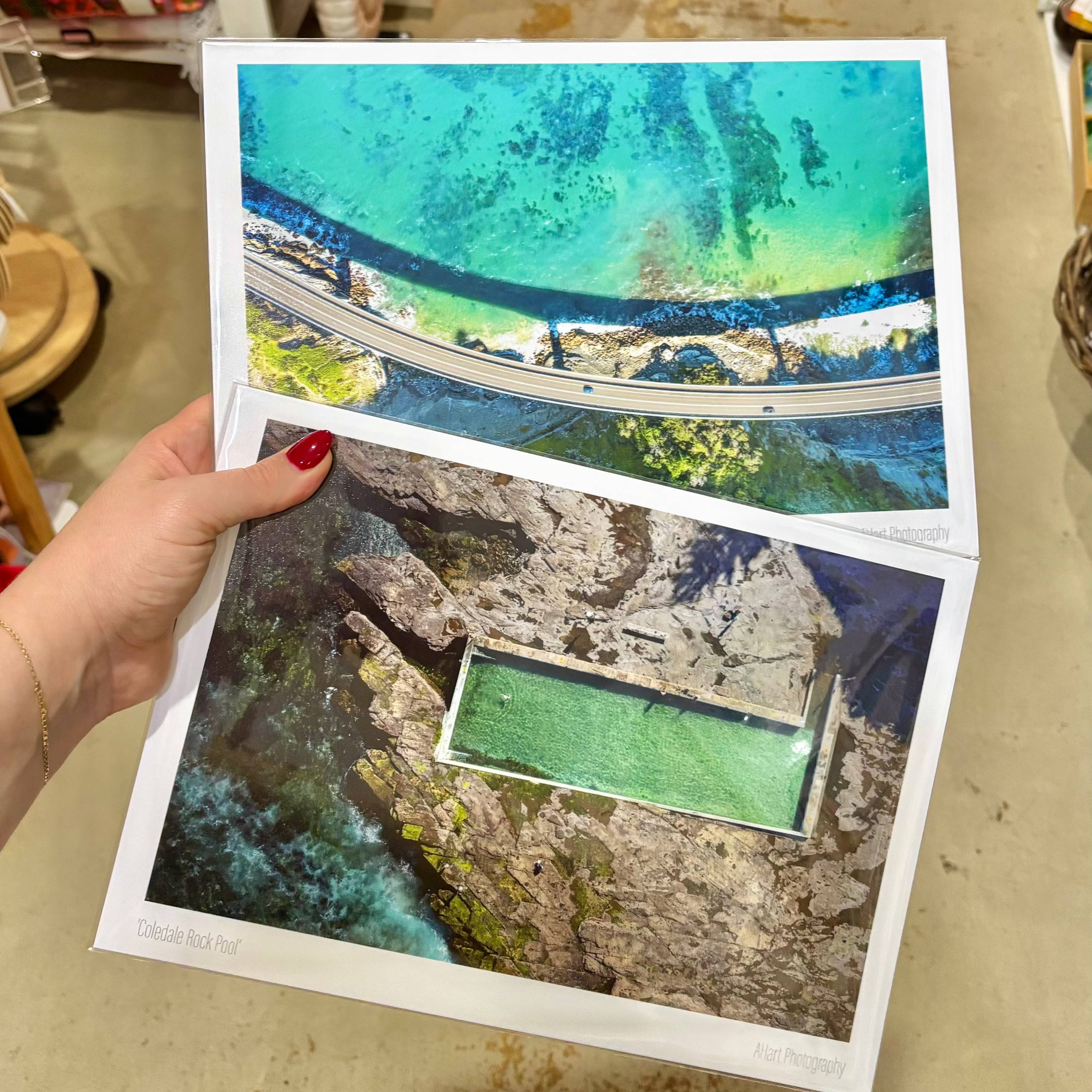 Two aerial photographs of a coastal area held by a hand. Two Ilawarra prints from Coledale Rock Pool and Sea Cliff Bridge Clifton NSW. Beautiful ocean photography from the south coast.